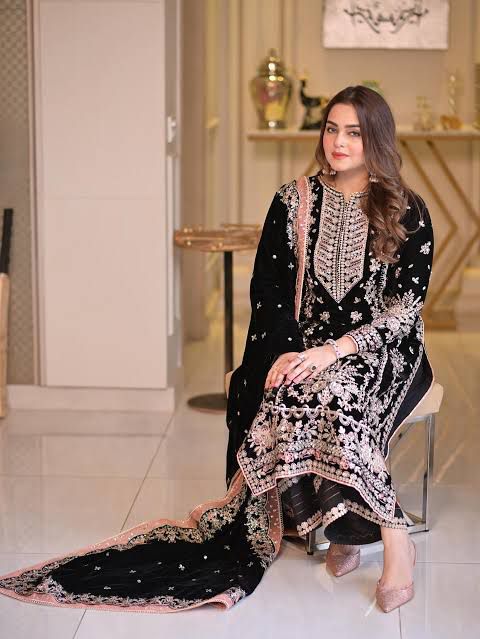 Woman in a black and white embroidered traditional outfit sitting on a chair.