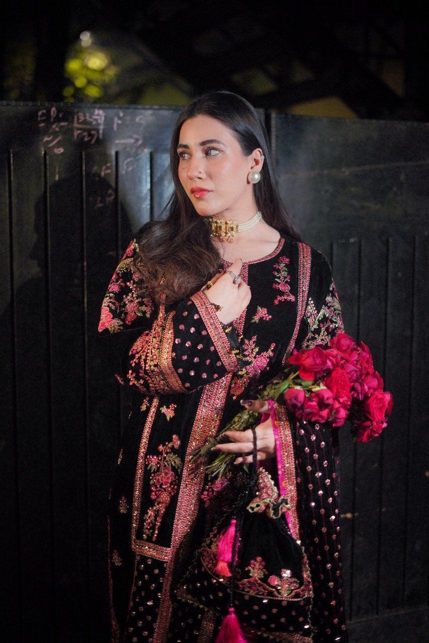 Woman in a black and red traditional outfit holding flowers against a dark background