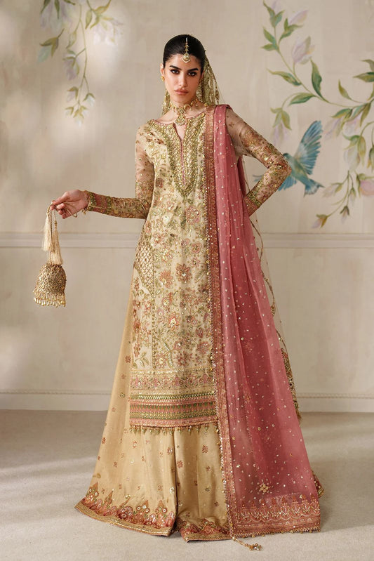 Woman in traditional embroidered outfit with pink dupatta against a decorative wall.