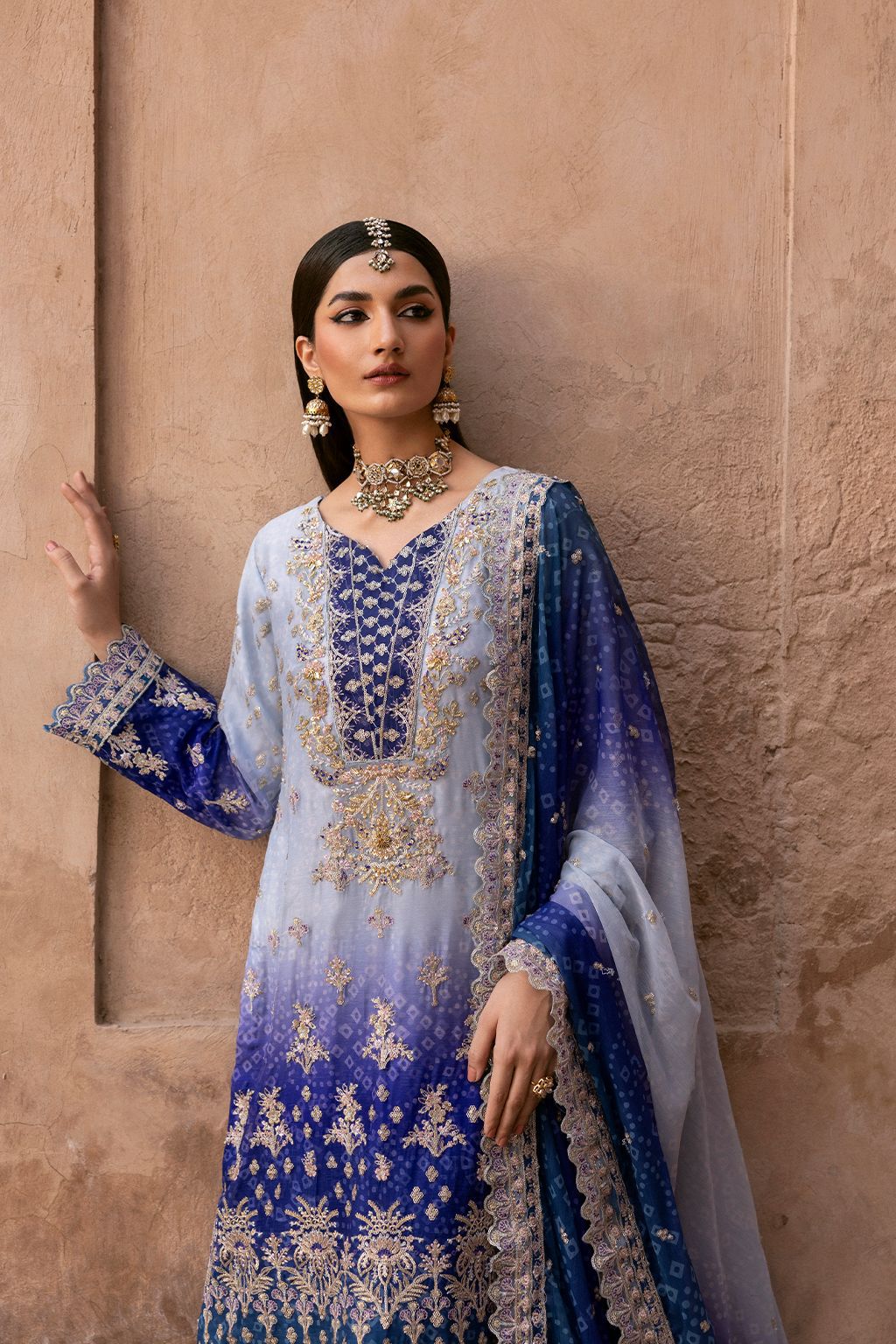 Emaan Adeel Tie Die blue and white embroidered traditional outfit against a beige wall.