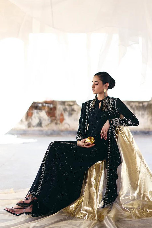 Woman in a black and gold traditional outfit sitting on a white surface with a blurred background