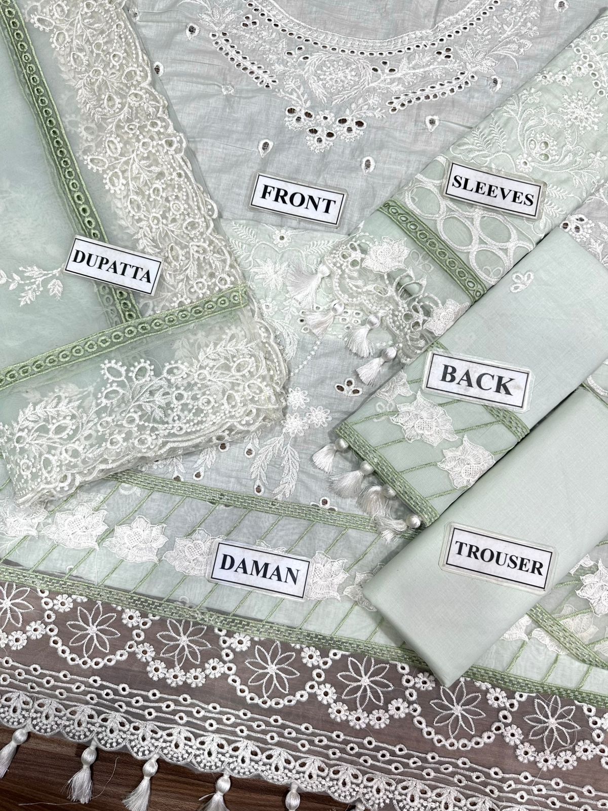 Embroidered fabric set with labels indicating parts of a traditional outfit on a wooden surface.