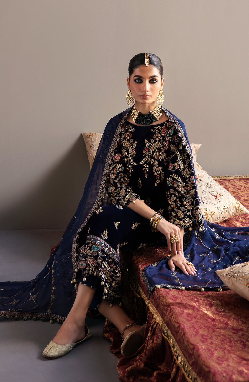 Emaan Adeel  Velvet  Woman in traditional attire sitting on a decorative couch against a plain background