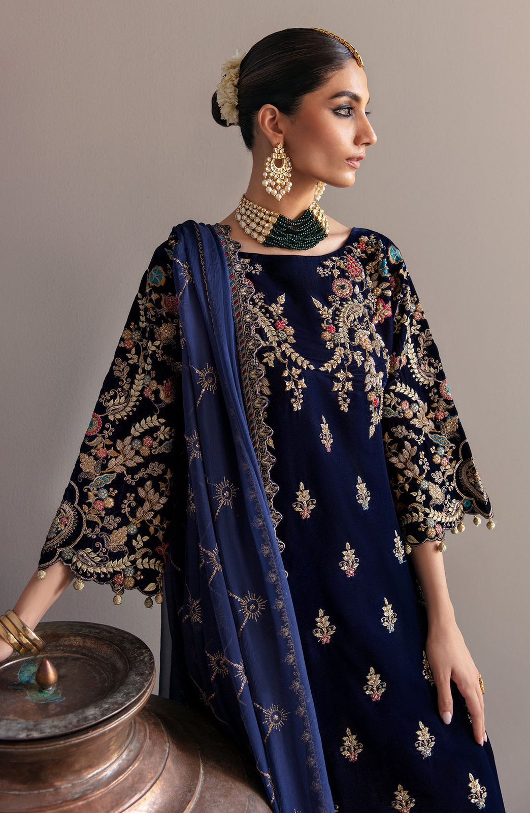 Emaan Adeel  Woman wearing a navy blue embroidered outfit with gold details on a gray background