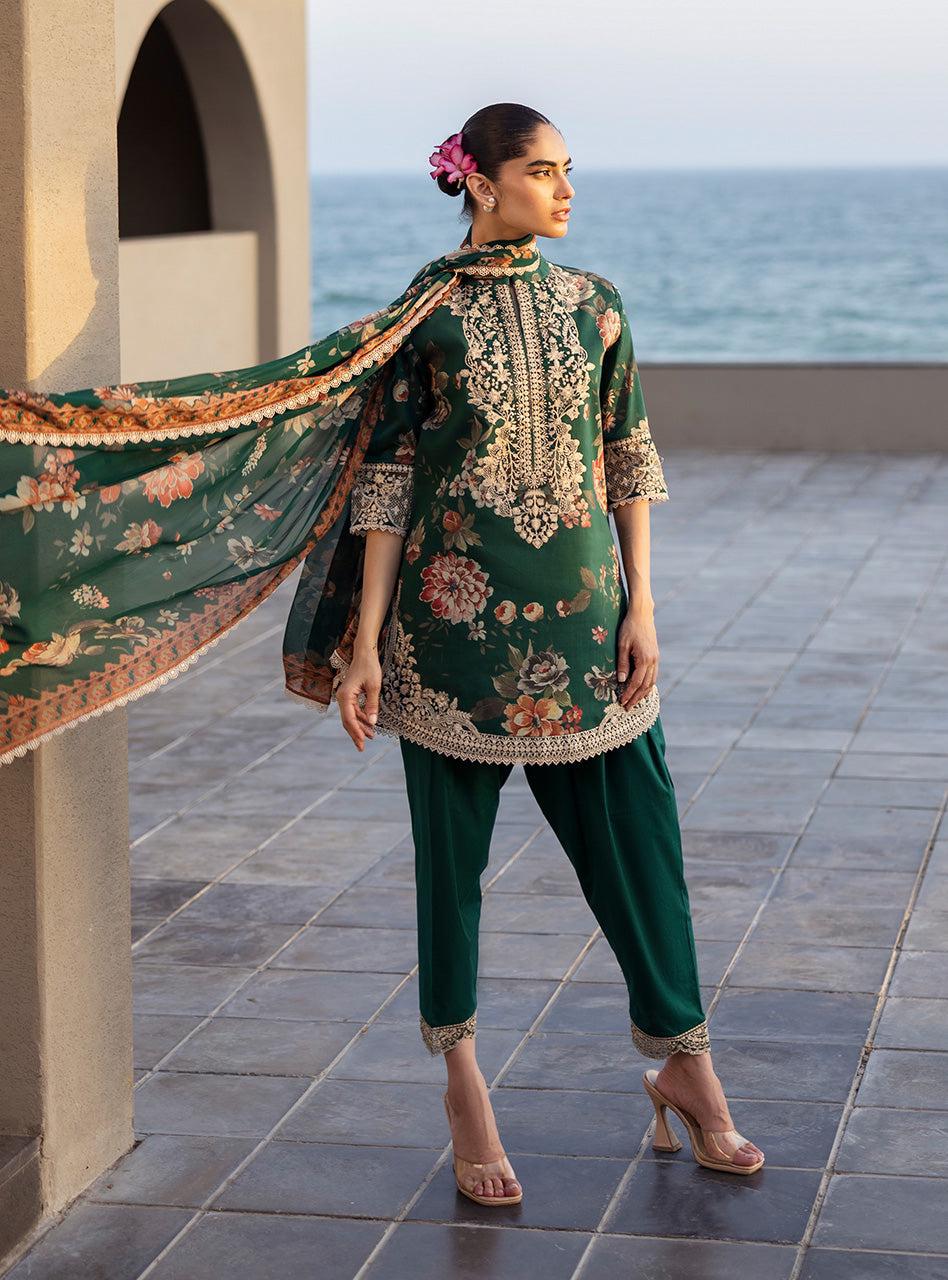 Zainab Chottani PAkistani Dress Woman in traditional green outfit with floral patterns standing on a tiled floor by the sea.