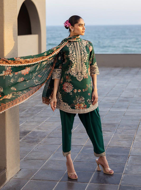 Zainab Chottani PAkistani Dress Woman in traditional green outfit with floral patterns standing on a tiled floor by the sea.