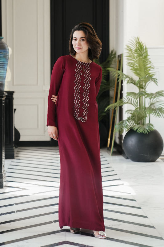 Woman in a burgundy Mehroon Silk dress  with white embroidery standing in an elegant interior setting.