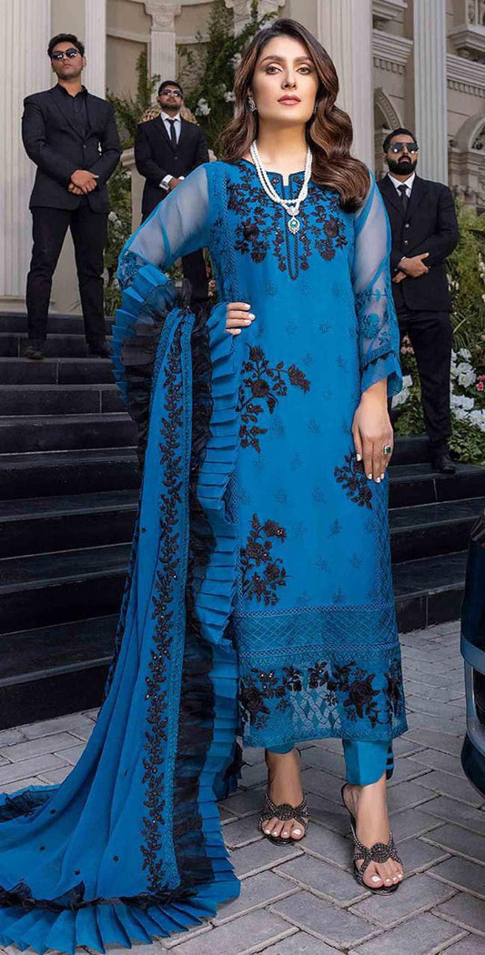 Azure in a blue embroidered outfit standing outdoors with people in formal attire in the background.