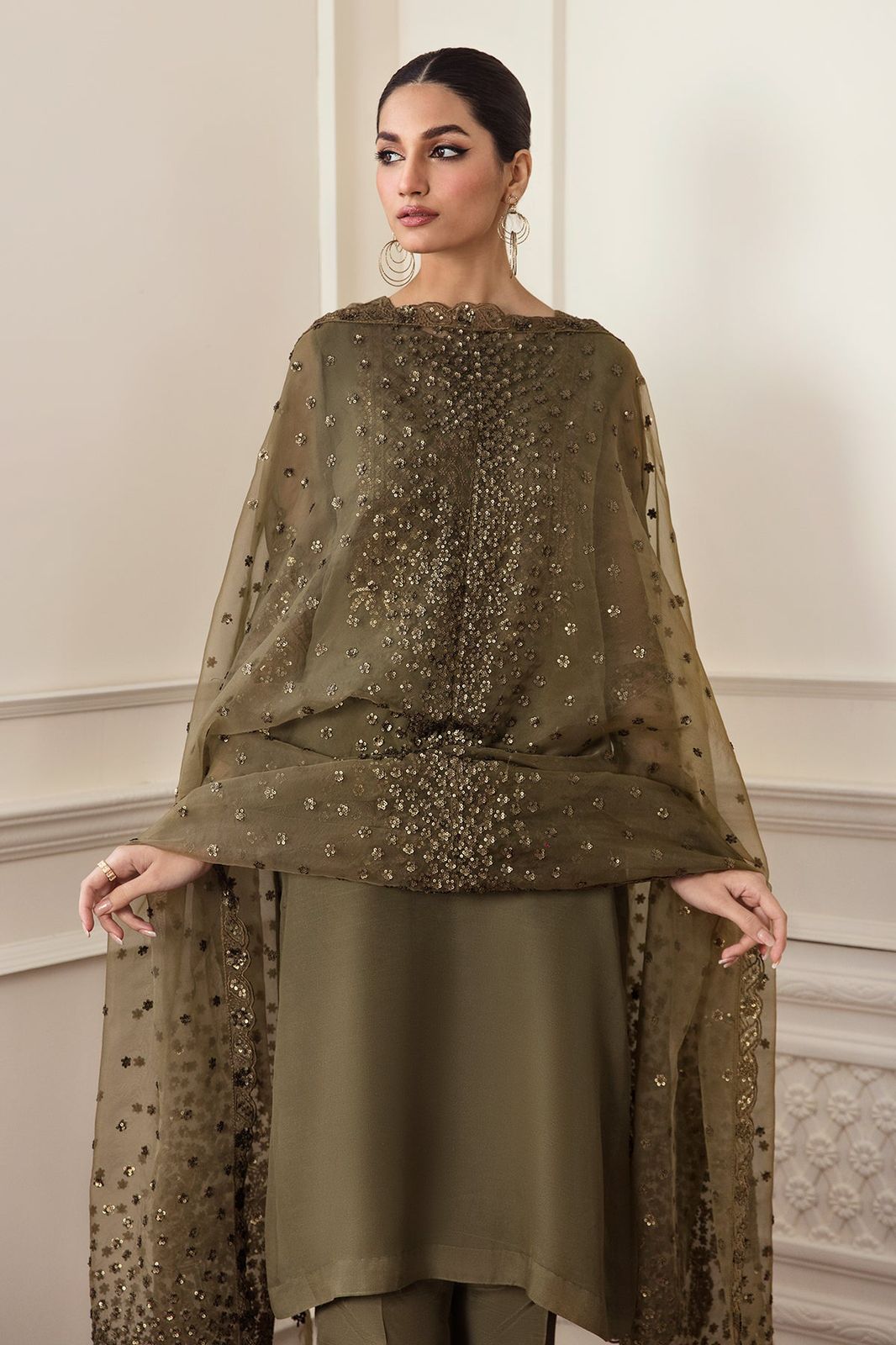 Woman wearing an olive green outfit with sequin detailing in a formal setting.