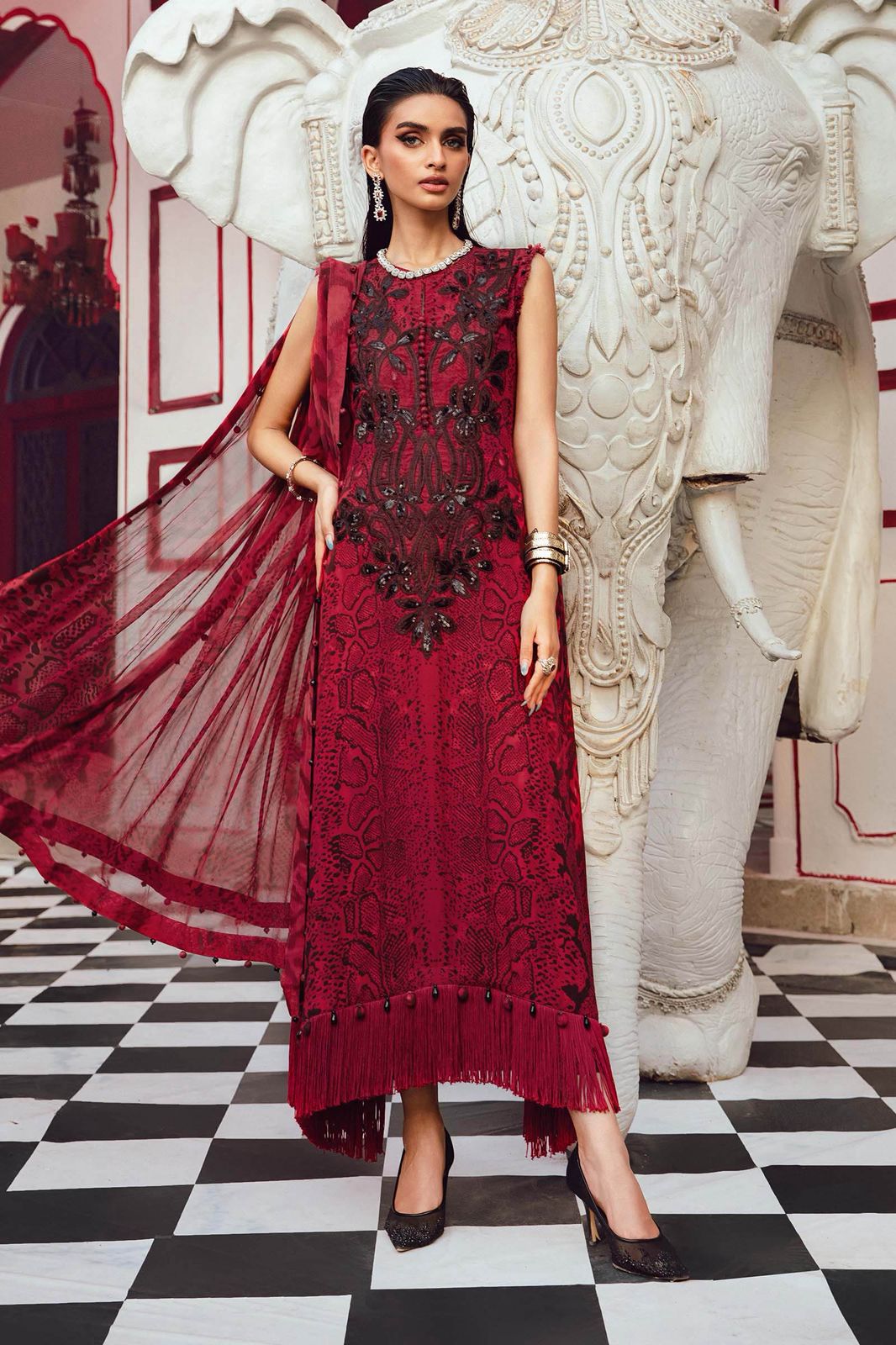 Maria b M print in a red embroidered dress standing next to a large decorative elephant statue.